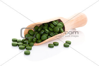 Green pills on wooden scoop.