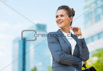Smiling business woman with briefcase in office district looking
