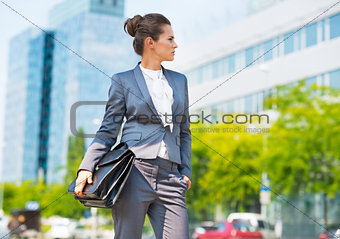 Happy business woman with briefcase in office district looking o