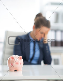 Closeup on piggy bank and frustrated business woman in backgroun