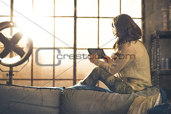 Young woman using tablet pc in loft apartment. rear view
