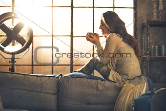 Young woman enjoying cup of hot beverage in loft apartment
