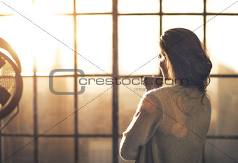Young woman enjoying cup of coffee in loft apartment. rear view