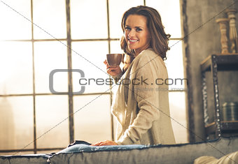 Happy young woman enjoying cup of coffee in loft apartment