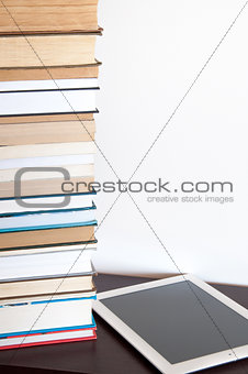 E-book reader and stack of books on a table