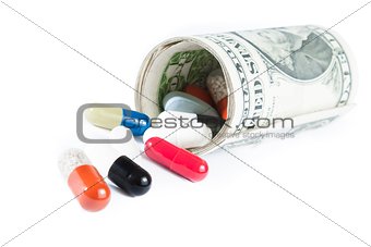 colorful pills in front of rolled up dollars on white background