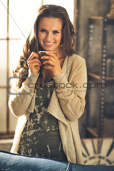 Portrait of smiling young woman with cup of coffee in loft apart