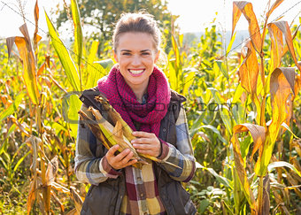 Happy young woman holding corn while standing in cornfield