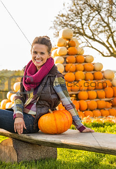 Portrait of happy young woman sitting with pumpkin in front of p