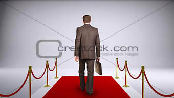 Businessman in suit holding briefcase and go forward on red carpet. Rear view