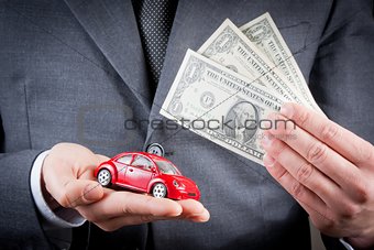 toy car and dollars in the hands of business man concept for insurance, buying, renting, fuel or service and repair costs 