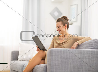 Happy young woman sitting on divan and using tablet pc