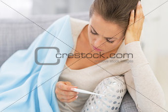 Portrait of ill young woman laying on couch and looking on therm