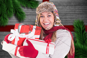 Composite image of happy blonde in winter clothes holding gifts