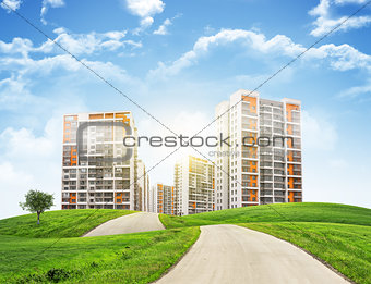 Tall buildings, green hills and road against sky with clouds