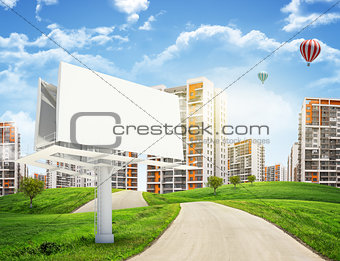 Tall buildings, green hills and road with large billboard against sky