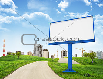 Tall buildings, green hills and road with large billboard against sky