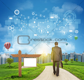 Businessman walks on road. Rear view. Buildings, grass field, wooden signboard and sky with virtual elements