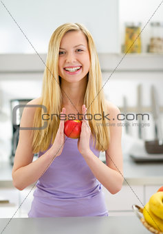 Portrait of smiling young woman with apple in kitchen