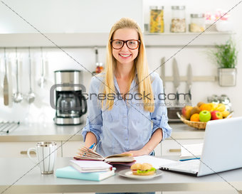 Portrait of happy young woman studying in kitchen