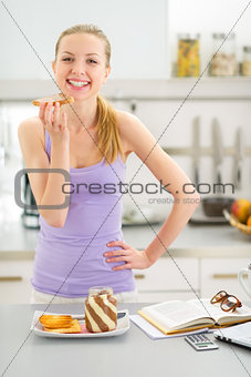 Happy teenager girl eating toast with chocolate cream in kitchen