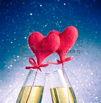 champagne flutes with golden bubbles and red velvet hearts make cheers on blue bokeh background