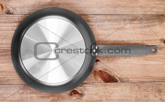 Frying pan on wooden table background. View from above