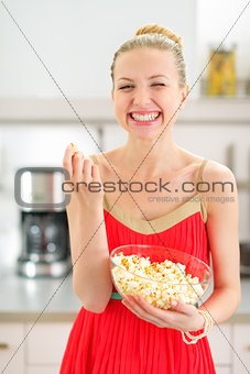 Portrait of smiling young woman eating popcorn in kitchen