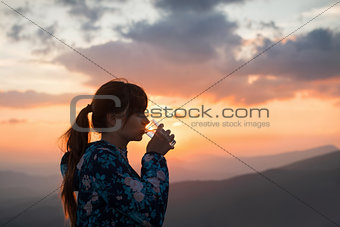 Woman drinking water on sunset background