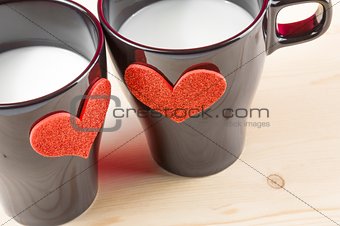 cups of milk with decorative hearts on wood table, concept of valentine day
