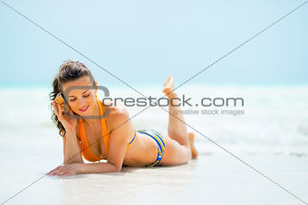 Young woman laying on beach and listening sound of sea in shell