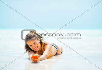 Young woman with shell laying on sea shore