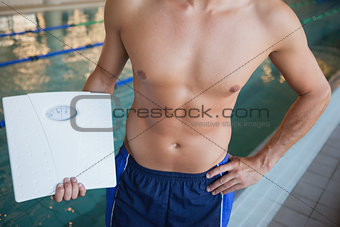 Mid section of a shirtless fit swimmer with weighing scales by pool