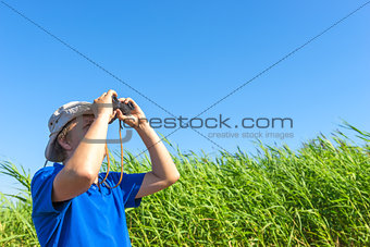 man looks for through the reeds with binoculars