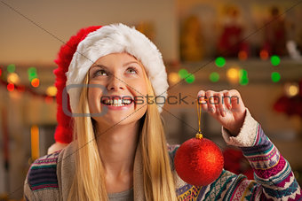 Happy teenager girl in santa hat holding christmas ball and look