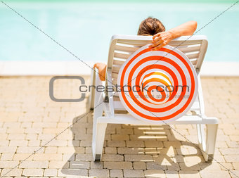 Young woman with hat laying on chaise-longue. rear view