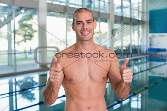 Fit swimmer gesturing thumbs up by pool at leisure center