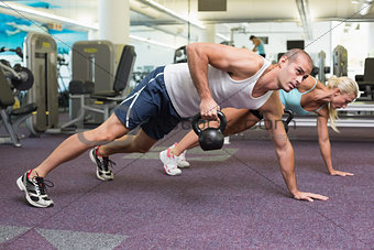 Fit couple doing push ups with kettle bells in gym