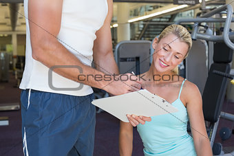 Woman discussing her performance on clipboard with a trainer at gym