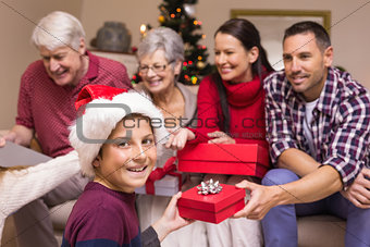 Smiling son exchanging gift with his family behind