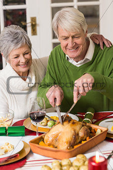 Man carving chicken while his wife having arm around him