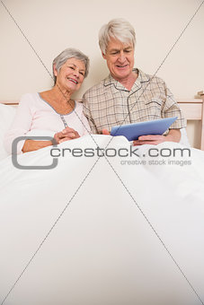 Senior couple relaxing in bed using tablet pc