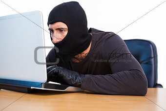 Burglar with balaclava hacking a laptop