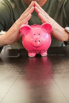 Mid section of a man with joined hands on piggy bank