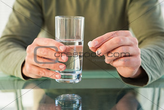 Close up of man holding a pill and glass of water