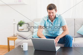 Smiling man at home on a laptop