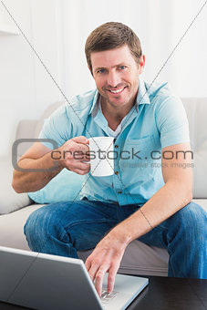Smiling man with a mug using a laptop