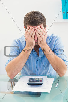 Stressed businessman covering his face at his desk