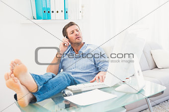 Businessman on the phone using his computer with his feet up
