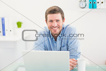 Smiling businessman holding mug at desk